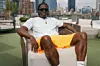 Saleem Gyau in a white shirt and colorful shorts lounges in a chair with the new york city skyline in the background.
