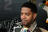 Kid Cudi leans back in a chair wearing a leather jacket.