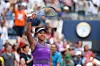 Naomi Osaka raises her tennis racket and is wearing a purple tennis uniform.