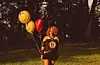 A young woman in a Bruins jersey holding baloons.