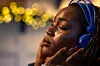 A close-up shot of a neurodiverse woman with AuDHD relaxing in a cozy, softly lit space, listening to music through noise-cancelling headphones. Surrounded by warm lights, she finds peace and grounding in her own way. This image celebrates the importance of quiet places and sensory-friendly environments in supporting neurodiverse individuals. Videos are available similar to this scenario.