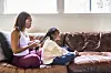 Mother brushing her daughters hair on couch at home