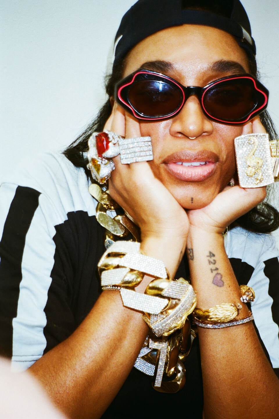 Person in sunglasses and cap showing large gold rings and bracelets