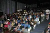 Large audience seated in a dimly lit conference auditorium