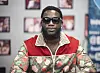 Gucci Mane seated at a table in a red and green patterned jacket and sunglasses at DBS Sounds event