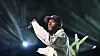 6lack performs with microphone amid bright stage lights at an indoor concert.