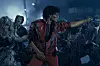 Jaafar Jackson in a red jacket dances among zombie performers on a dark street set