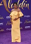 Tatyana Ali stands on a purple carpet in a strapless yellow gown at Disney’s Aladdin premiere.