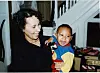 Woman holding a smiling young child indoors near stairs and a window.