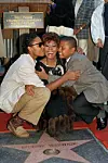 Woman kneels between two children beside a Walk of Fame star and a Hollywood Chamber of Commerce sign.