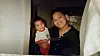 Adult holding a smiling child indoors near a doorway with curtains.