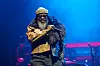 Black Thought of The Roots performs onstage beneath blue lights at a music festival.