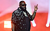 Rick Ross performs onstage in a star-patterned shirt with red lights behind him.
