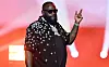Rick Ross performs onstage in a star-patterned shirt with red lights behind him.