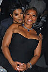 Teyana Taylor stands behind Queen Latifah as they pose together in black eveningwear at a gala event.