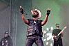 JPEGMAFIA performs onstage at Lollapalooza with a microphone, band members, and green stage lighting.