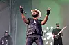 JPEGMAFIA performs onstage at Lollapalooza with a microphone, band members, and green stage lighting.
