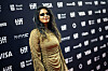 M.I.A. stands on the TIFF red carpet in a gold dress before a sponsor logo backdrop.