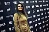 M.I.A. stands on the TIFF red carpet in a gold dress before a sponsor logo backdrop.