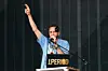 A person in a blue shirt speaks at a podium with an iPeriod logo and raises one hand.
