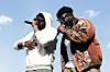 Two performers holding microphones and singing outdoors under a clear sky.