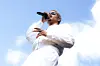 Performer in white singing into a microphone outdoors under a blue sky.