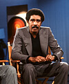 Richard Pryor seated in a studio chair against a blue background.