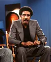 Richard Pryor seated in a studio chair against a blue background.