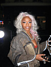 Person with platinum-blonde hair wearing an oversized jacket stands outdoors at night.