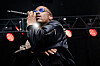Vince Staples sings into a microphone onstage with red lights glowing behind him.