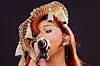 Singer wearing an elaborate headpiece performs into a microphone on a dark stage.