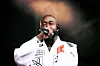 Singer in a white jacket performing with a microphone on a dimly lit stage.