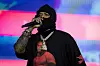 Westside Gunn performs on stage under pink and blue lights, wearing a black hoodie and mask.
