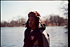 Person wearing a hooded winter jacket and fur hat standing by a frozen waterway.