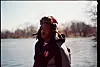 Person wearing a hooded winter jacket and fur hat standing by a frozen waterway.