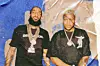 Two men in black shirts and chain necklaces pose in front of a blue backdrop.