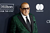 Clive Davis in a green sequined jacket at a GRAMMY gala step-and-repeat with Hilton and Mastercard logos.