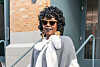Lauryn Hill stands outside a venue wearing sunglasses, a gray-and-white outfit, and gold earrings during New York Fashion Week.