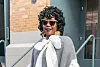 Lauryn Hill stands outside a venue wearing sunglasses, a gray-and-white outfit, and gold earrings during New York Fashion Week.