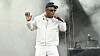 T.I. performs on a smoky outdoor stage, wearing white and holding a microphone.