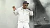 T.I. performs on a smoky outdoor stage, wearing white and holding a microphone.