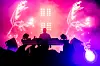Silhouetted DJ on stage in front of bright pink and purple concert lights.