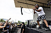 Lupe Fiasco performs on an outdoor stage while fans raise their hands in front of the barricade.