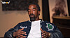 Man in a dark jacket with a Stüssy logo and Jets patch sits indoors and gestures while talking.