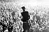 Silhouetted performer on stage facing a large illuminated concert crowd.