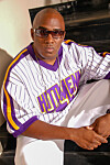 DJ Bigga Rankin sits wearing a purple and white jersey and sunglasses in a posed portrait.