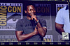 A man stands onstage holding a microphone during a San Diego Comic-Con panel.