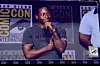 A man stands onstage holding a microphone during a San Diego Comic-Con panel.