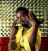 Man in a yellow shirt poses with hands raised in front of a shiny patterned background.
