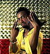 Man in a yellow shirt poses with hands raised in front of a shiny patterned background.